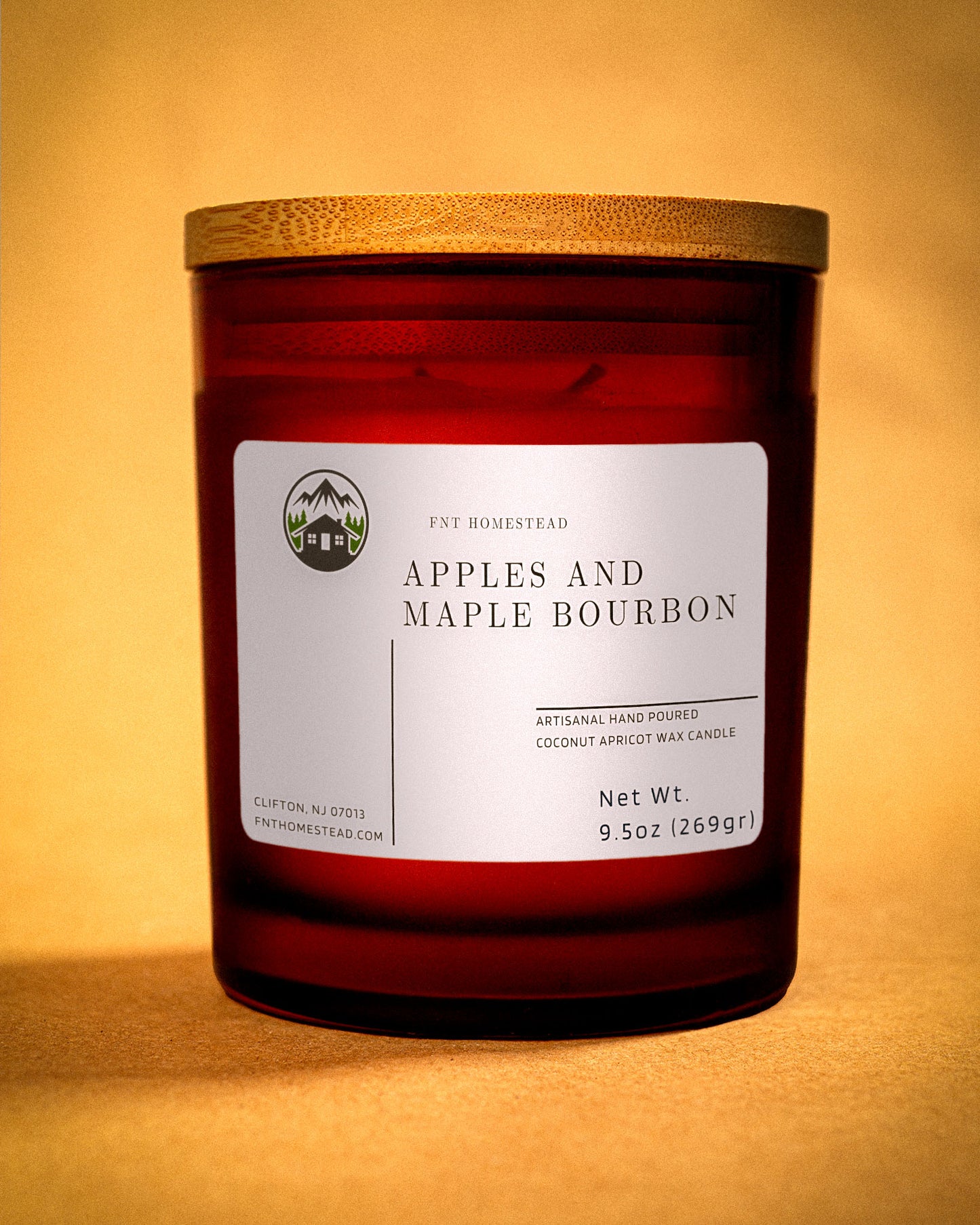 an amber jar candle with a wooden lid, labeled 'Apples and Maple Bourbon'. The label indicates it's an artisanal hand-poured candle made with coconut apricot wax.