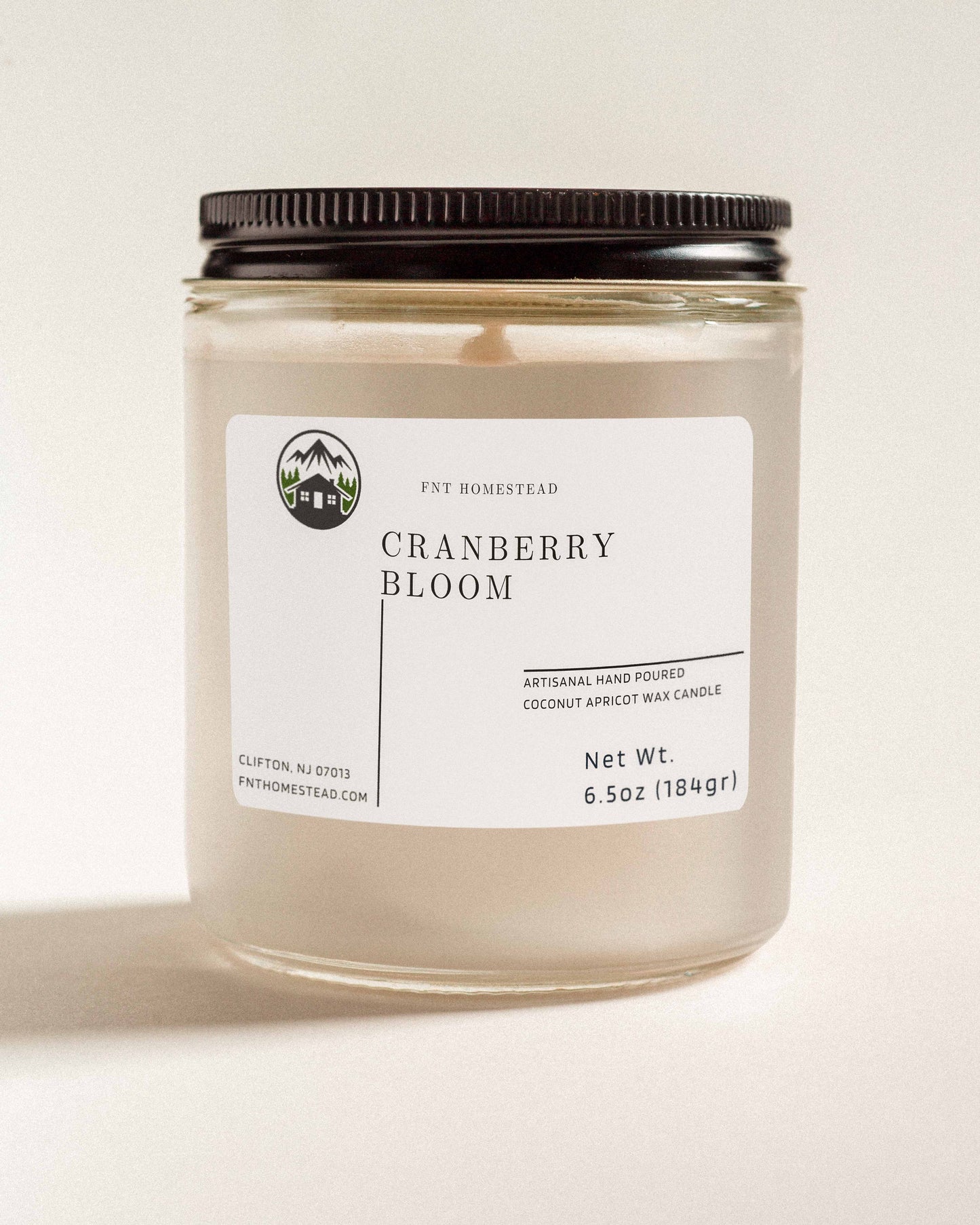 'Cranberry Bloom' scented candle in a clear glass jar with a black lid. This handcrafted candle features a smooth, white wax surface and is made with coconut apricot wax.