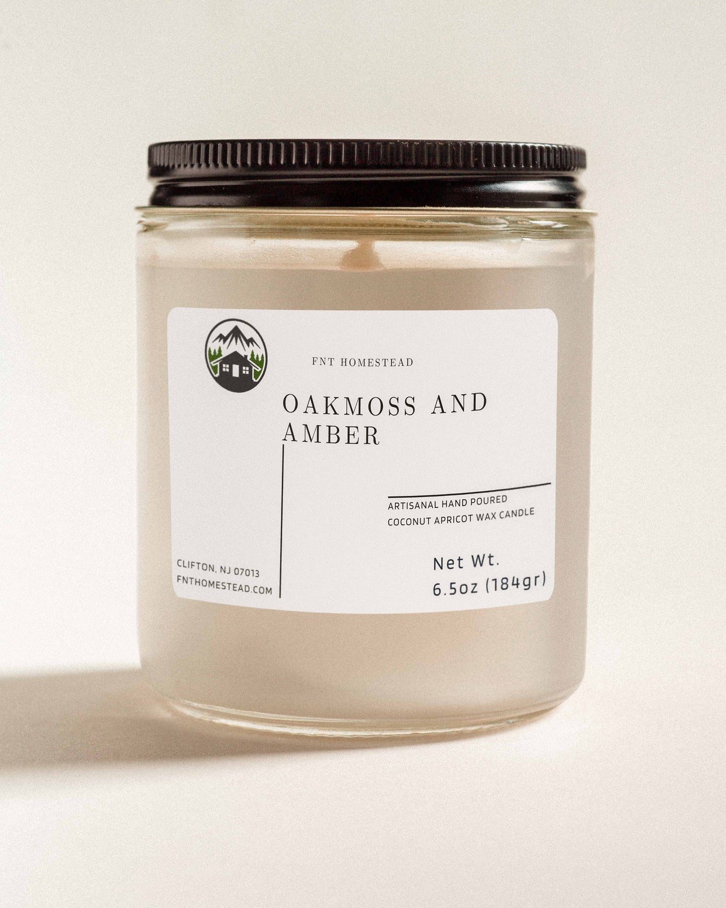 'Oakmoss and Amber' scented candle in a clear glass jar with a black lid. This handcrafted candle features a smooth, white wax surface and is made with coconut apricot wax.