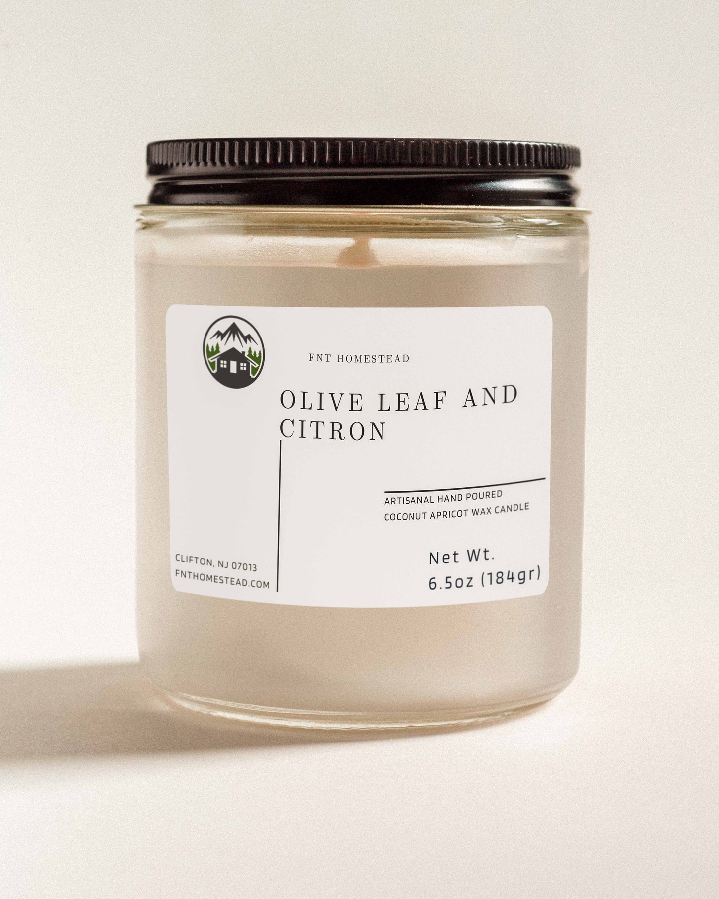 'Olive Leaf and Citron' scented candle in a clear glass jar with a black lid. This handcrafted candle features a smooth, white wax surface and is made with coconut apricot wax.