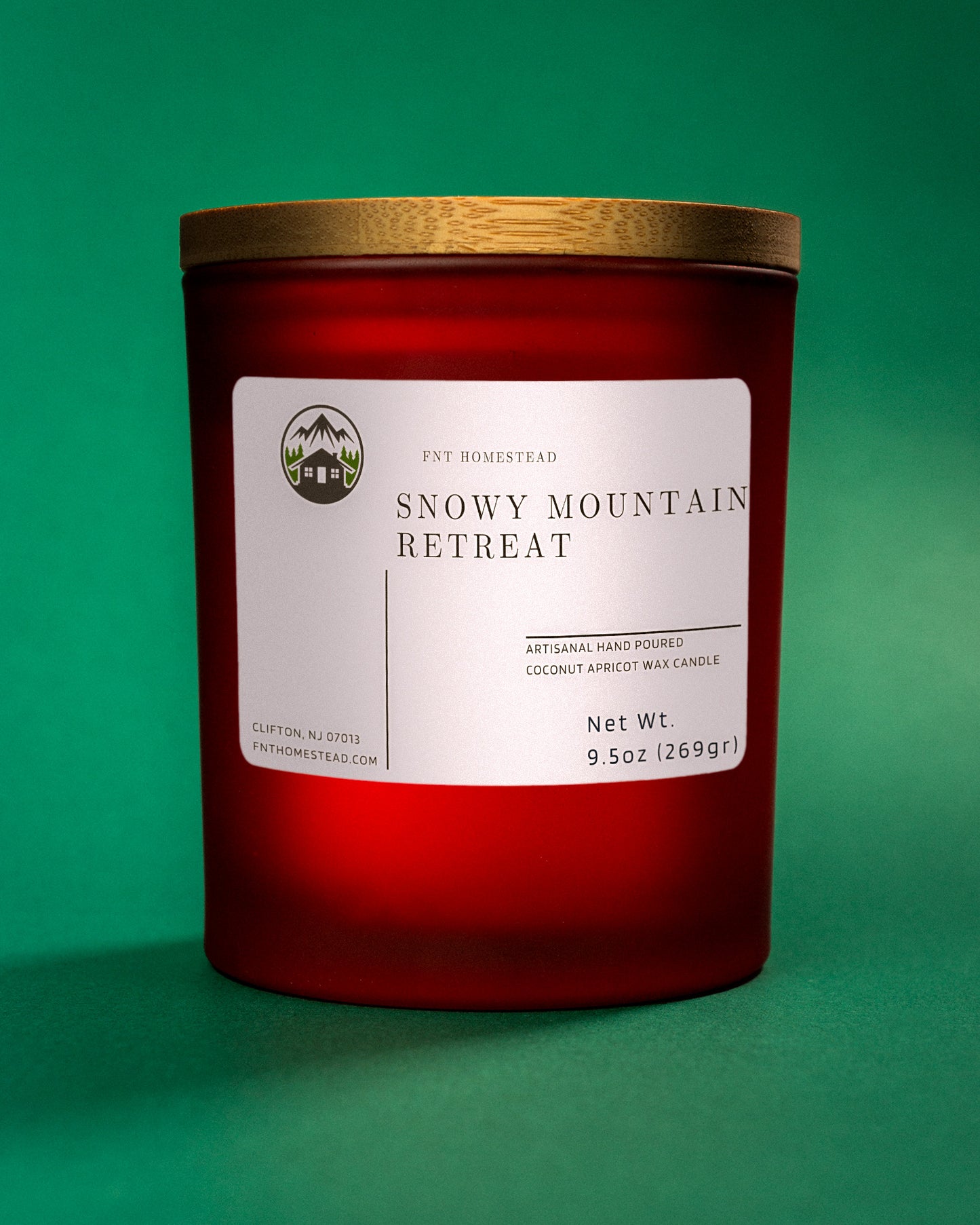 Close-up of a red 'Snowy Mountain Retreat' candle with a wooden lid. The label indicates it's an artisanal hand-poured candle made with coconut apricot wax.