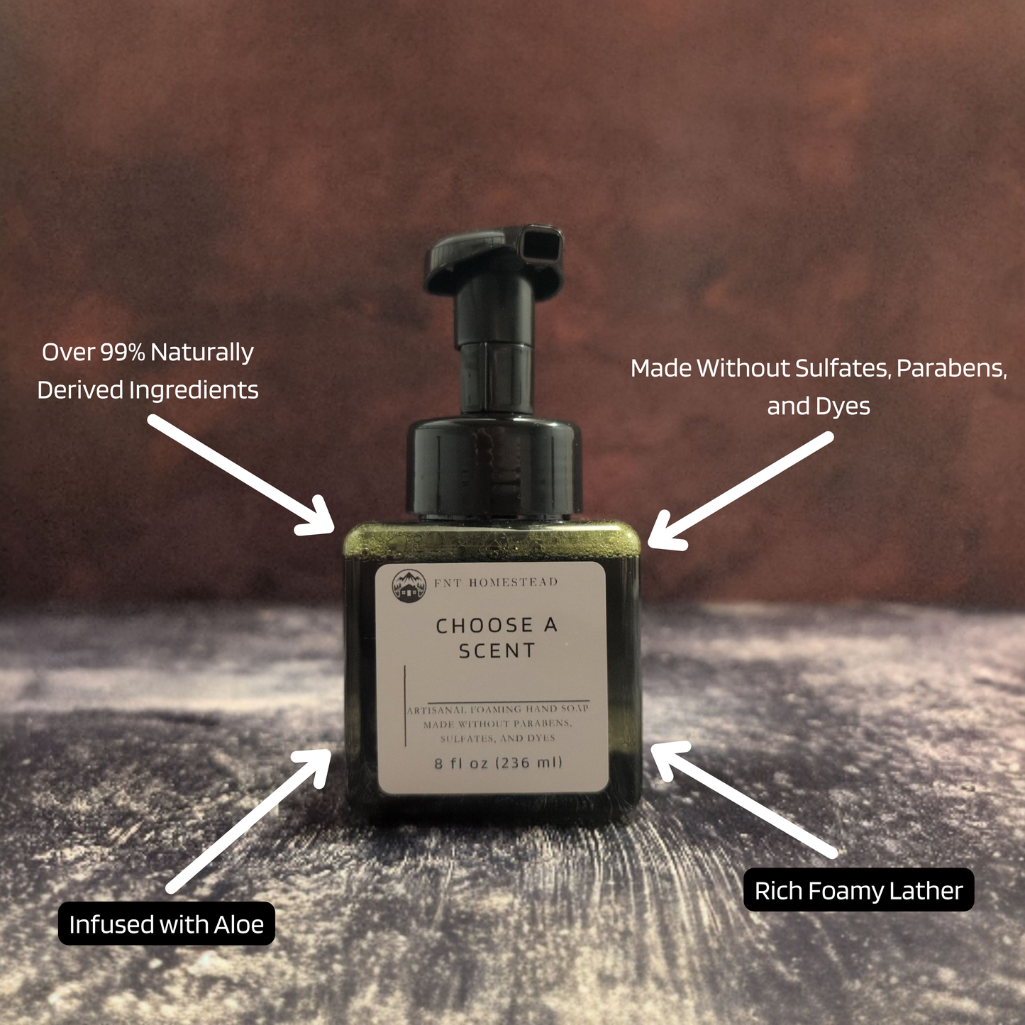 An infographic for FNT Homestead foaming hand soap. A photo of the dark green, square soap bottle is in the center against a dark, textured background. Four white arrows point to the bottle, each highlighting a feature with text in a black box: Top left: "Over 99% Naturally Derived Ingredients" Top right: "Made Without Sulfates, Parabens, and Dyes" Bottom left: "Infused with Aloe" Bottom right: "Rich Foamy Lather"