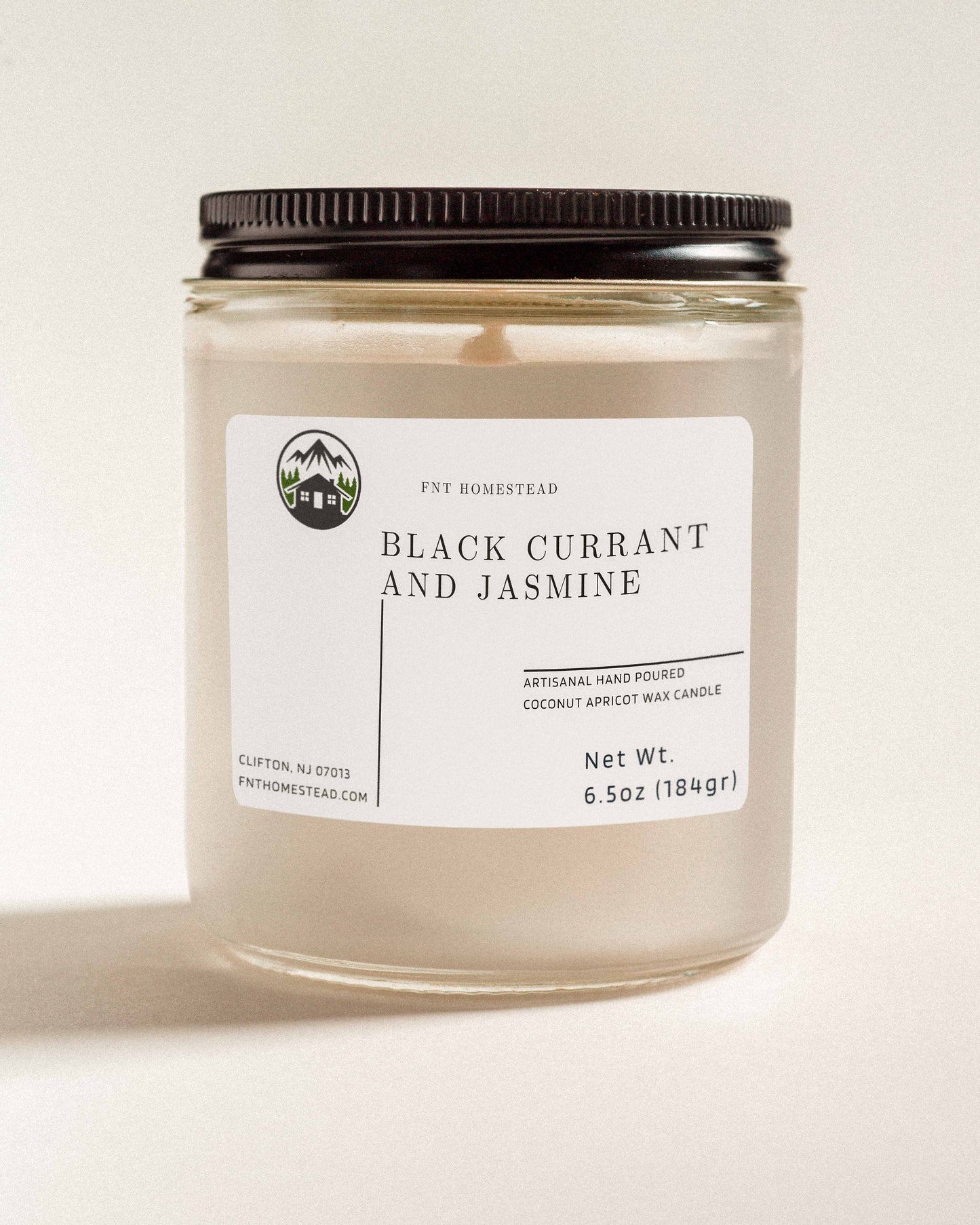 'Black Currant and Jasmine' scented candle in a clear glass jar with a black lid. This handcrafted candle features a smooth, white wax surface and is made with coconut apricot wax.