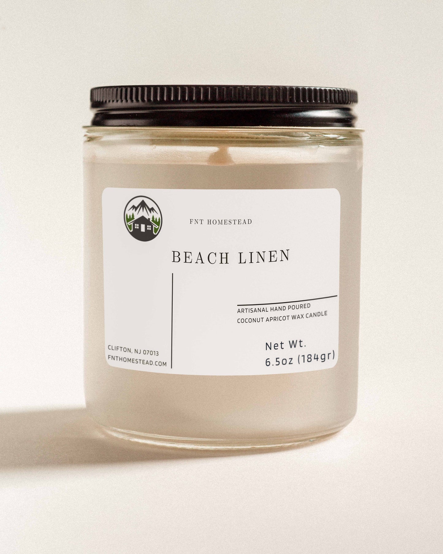 'Beach Linen' scented candle in a clear glass jar with a black lid. This handcrafted candle features a smooth, white wax surface and is made with coconut apricot wax.