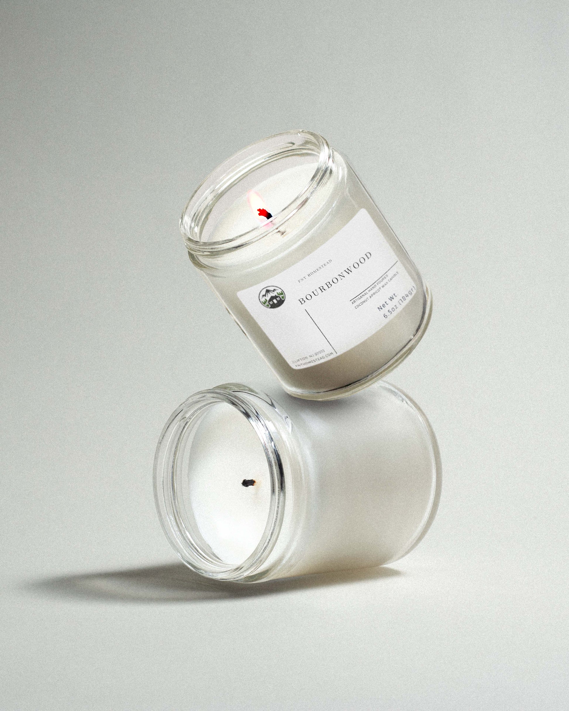 Two clear glass jar candles labeled 'Bourbonwood', one upright and one tilted standing on top of the upright in a playful manner, showcasing the clean fragrance and minimalist design.