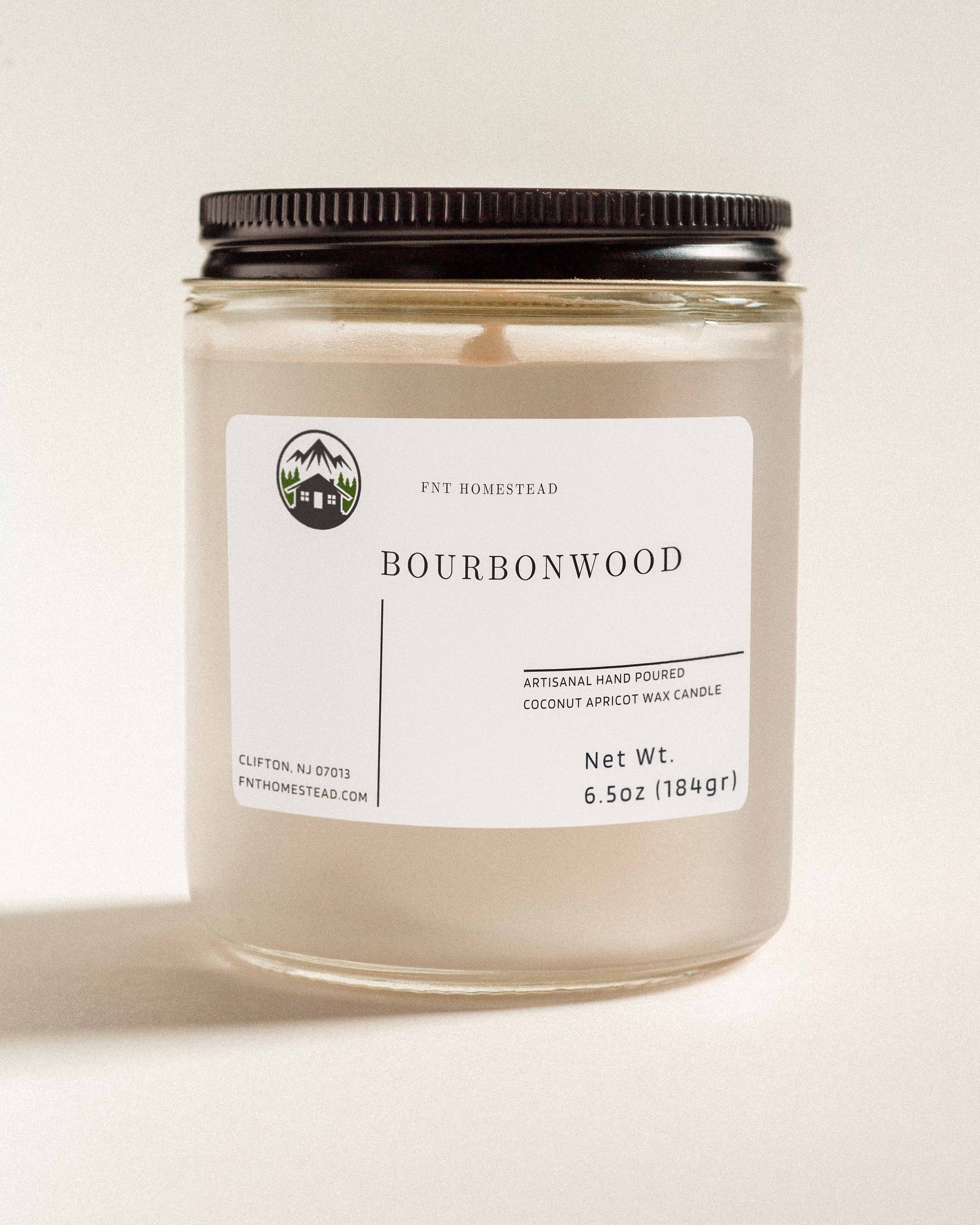 'Bourbonwood' scented candle in a clear glass jar with a black lid. This handcrafted candle features a smooth, white wax surface and is made with coconut apricot wax.