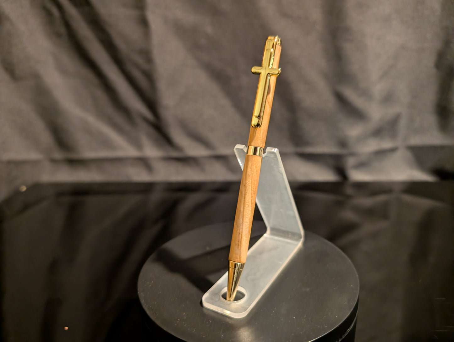 Wooden pen with gold accents on a clear stand against a dark background