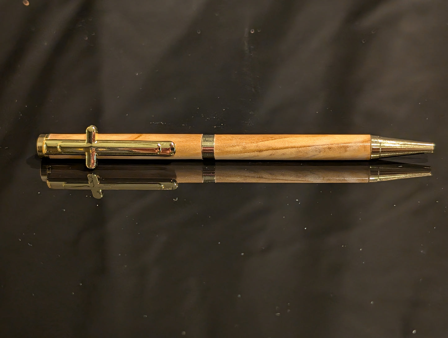 Wooden pen with gold accents on a reflective black surface