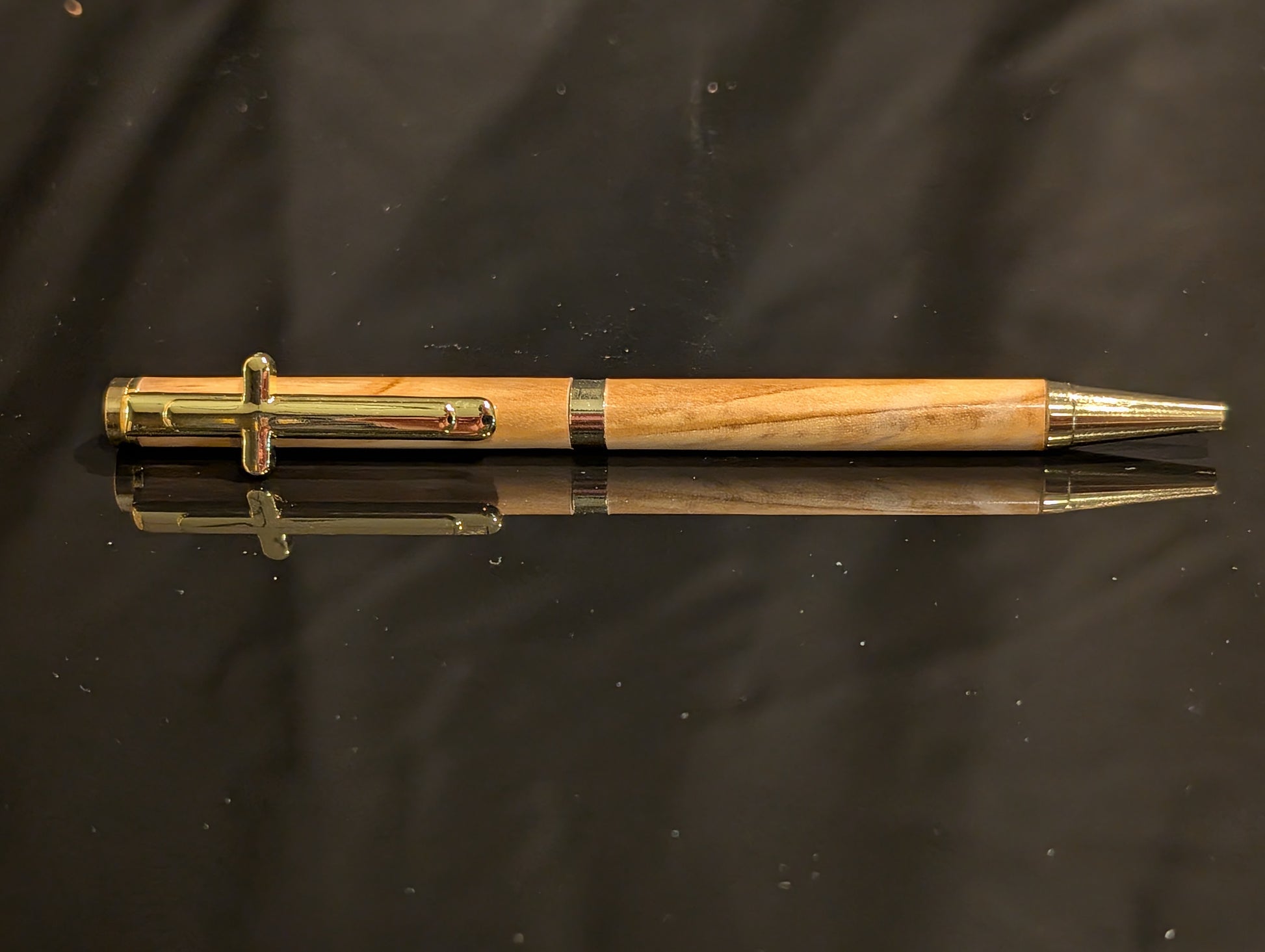 Wooden pen with gold accents on a reflective black surface