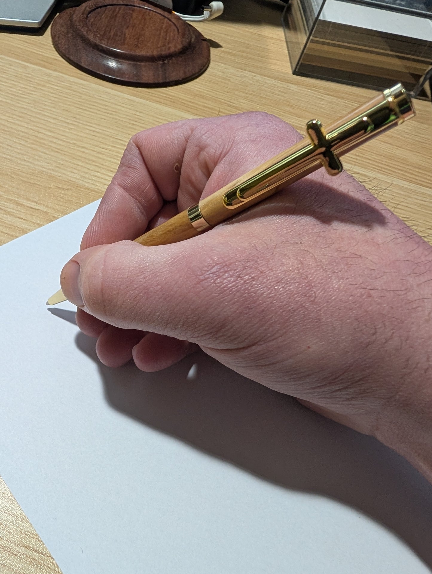 Hand holding a gold pen over a piece of paper on a wooden desk.