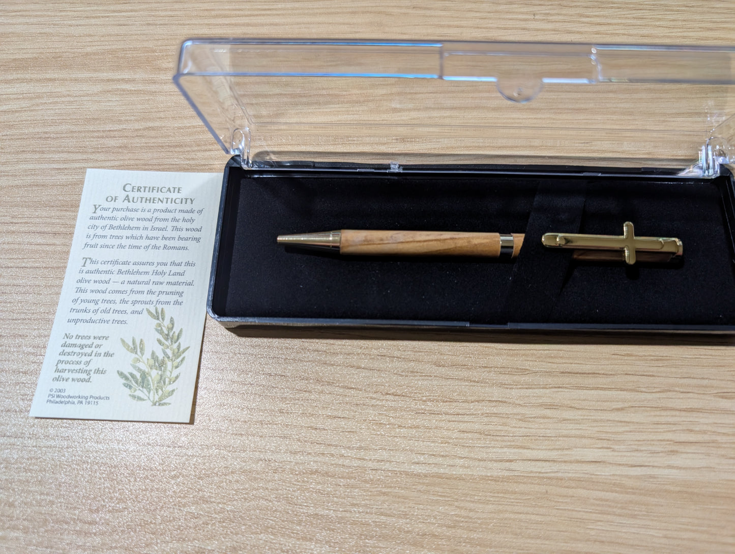 Wooden pen and gold tool in a clear box with a certificate of authenticity on a wooden surface