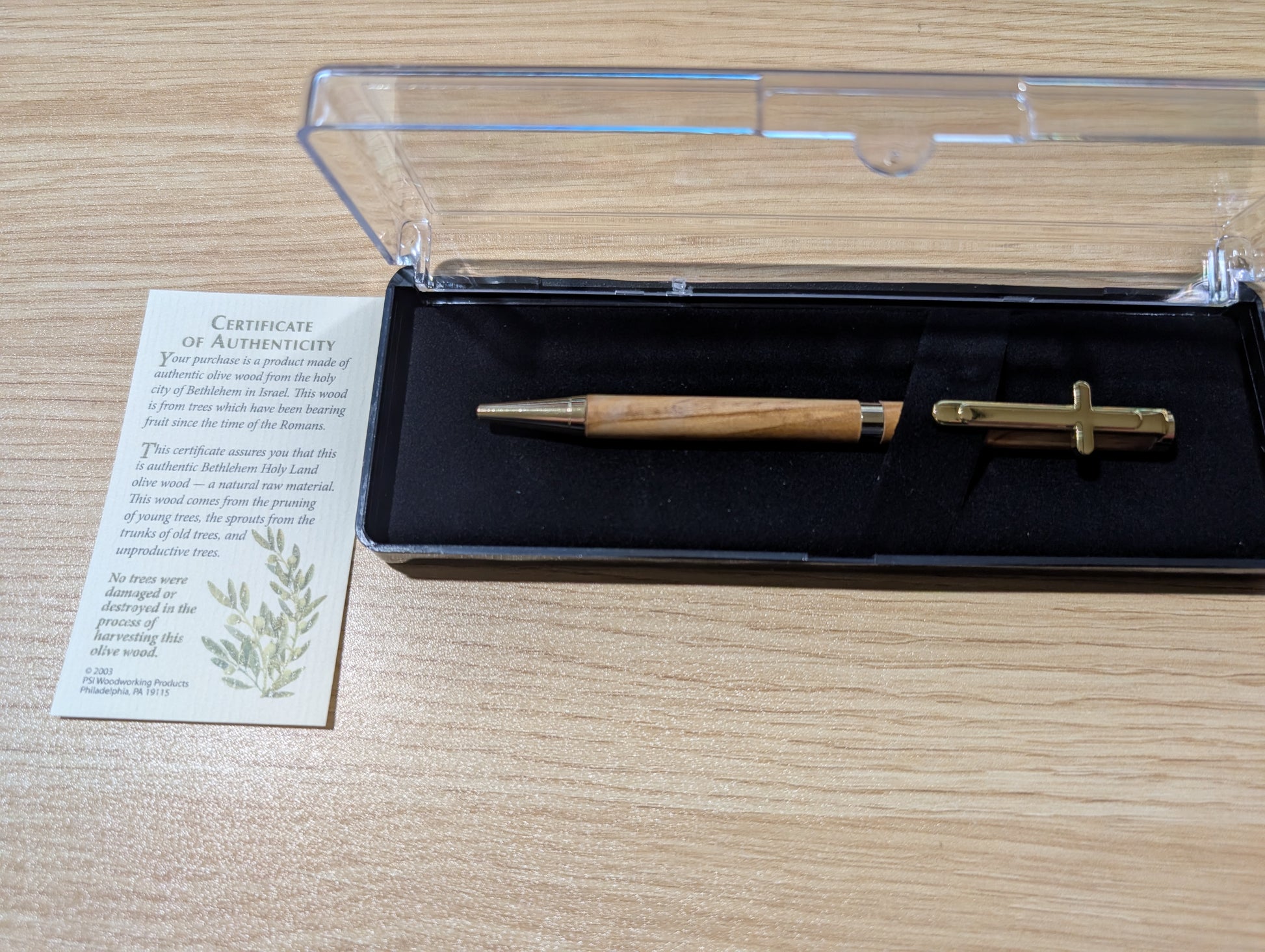 Wooden pen and gold tool in a clear box with a certificate of authenticity on a wooden surface