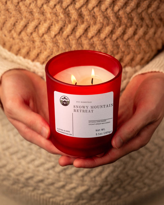 A person holds a glowing red jar candle called 'Snowy Mountain Retreat', creating a warm and inviting atmosphere.