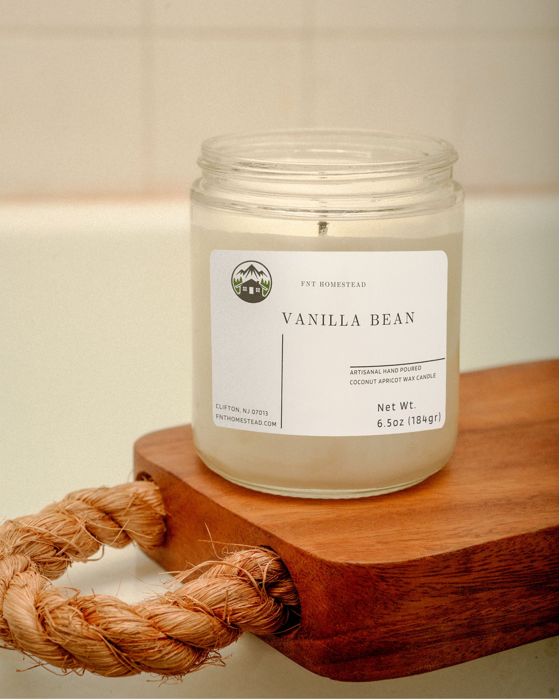 'Vanilla Bean' candle in a clear glass jar with a black lid. The candle is placed on a wooden surface with a coiled rope beside it. Its minimalist design complements any decor.